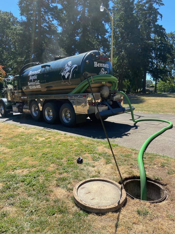 A septic service truck with hoses is parked by a manhole in a grassy area, actively performing septic tank maintenance.