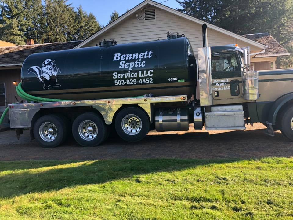 A Bennett Septic Service LLC vacuum truck is parked on a driveway in front of a house, with a green septic tank and company contact information on the side.